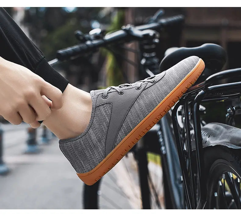 Men’s wide toe breathable mesh running sneakers in gray textured canvas with a contrasting orange rubber sole and black laces.