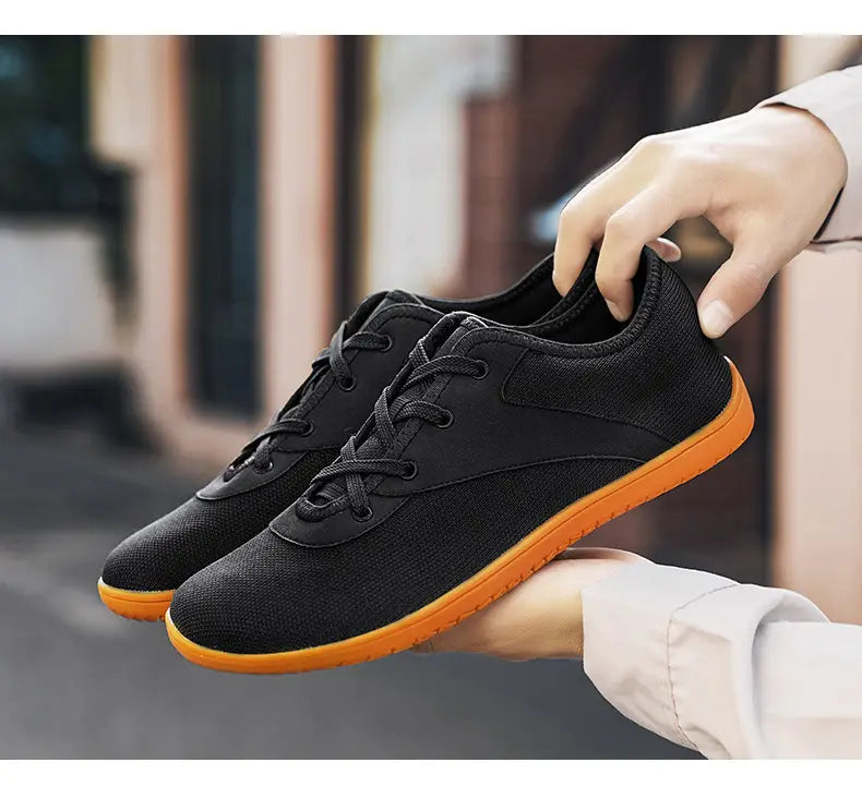 men’s wide toe breathable mesh running sneakers in black canvas with vibrant orange rubber sole and black laces shown from the back side