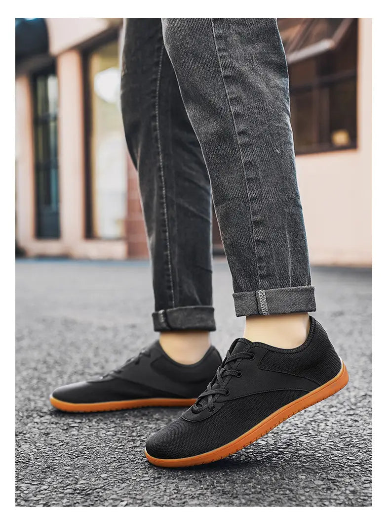 Men’s wide toe breathable mesh running sneakers in black canvas with a contrasting orange sole and black laces.