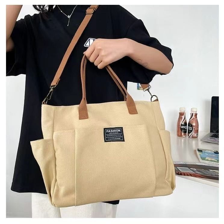 Beige canvas large capacity commuter tote with brown leather handles and shoulder strap featuring a black rectangular patch on the front.