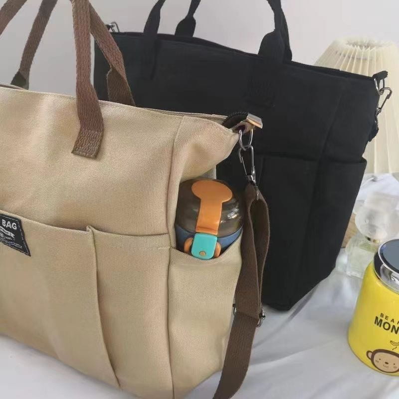 Beige large capacity canvas commuter tote with brown leather straps and a front pocket holding a water bottle.