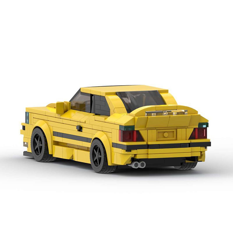 Modèle de voiture de sport en briques Lego E36 jaune éclatant, avec accents noirs et feux arrière détaillés, présenté depuis le côté arrière.