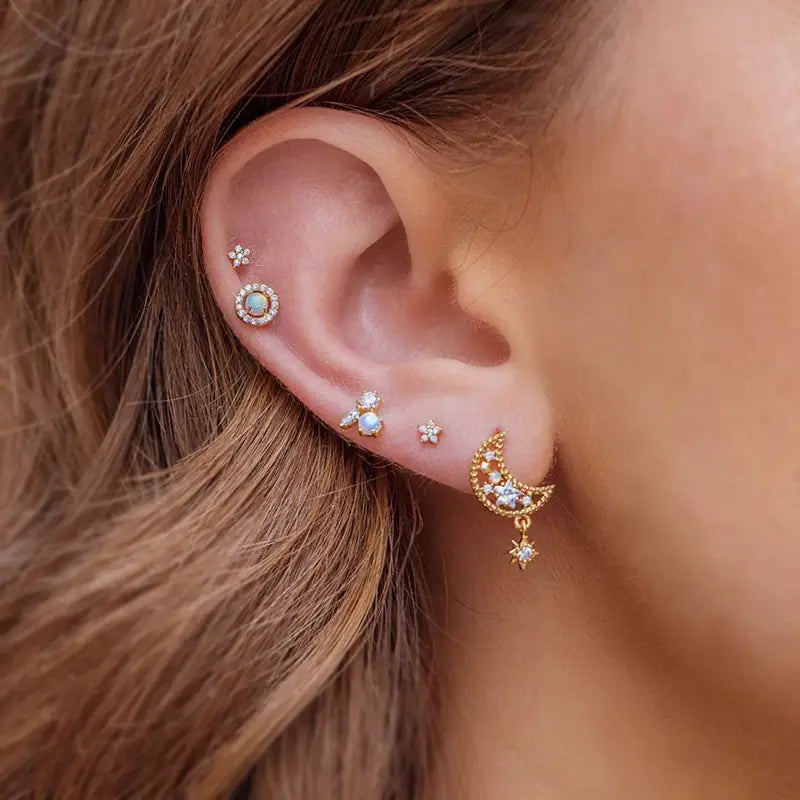 Ensemble boucles d’oreilles et manchettes « étoile et lune » en forme de papillon, comprenant des piercings d’oreille à thème céleste à finition dorée, avec un croissant de lune et une étoile suspendue entourée de petites étoiles, ainsi qu’un centre à l’aspect d’opale.