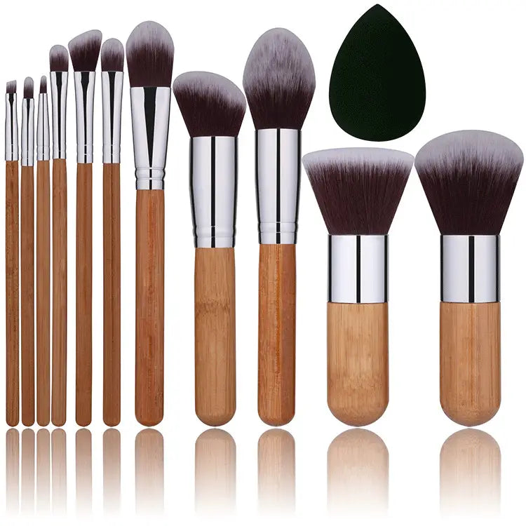 Bambus-Make-up-Pinselset mit 12 Pinseln mit Bambusgriff, silbernen Zwingen und dunkelbraunen bis grauen Farbverlaufborsten, ergänzt durch einen schwarzen tränenförmigen Schwamm.
