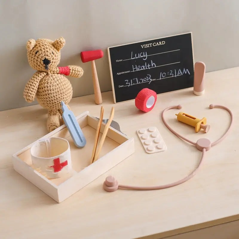 Osito de peluche tejido a crochet con cuerpo de hilo color beige y nariz negra bordada, con una pulsera tejida en punto acanalado color rojo, incluido en el set de juguete médico infantil de doctor de madera y silicona.