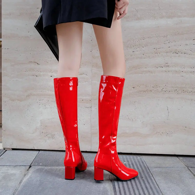 Bright red patent leather knee high boots with a glossy finish and block heel featuring a square toe design.