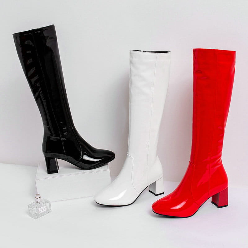 Three glossy patent leather knee high block heel square toe boots in black white and red displayed side by side.