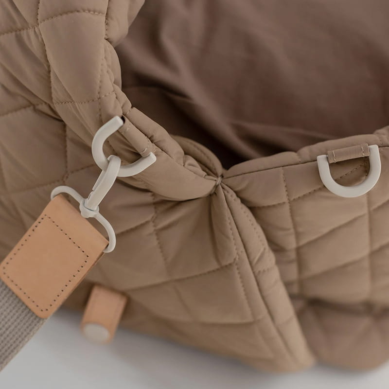 beige quilted travel pet carrier bag with puffer jacket style, white plastic hardware, and tan leather tag.