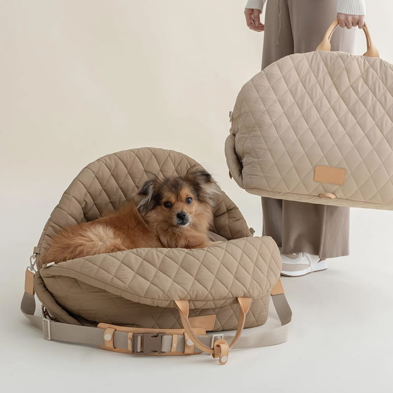 Beige quilted travel pet carrier bag with tan leather handles and adjustable straps.