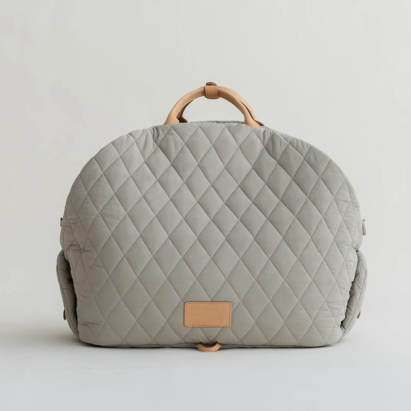 Gray quilted travel pet carrier bag with tan leather handles and a matching leather patch.