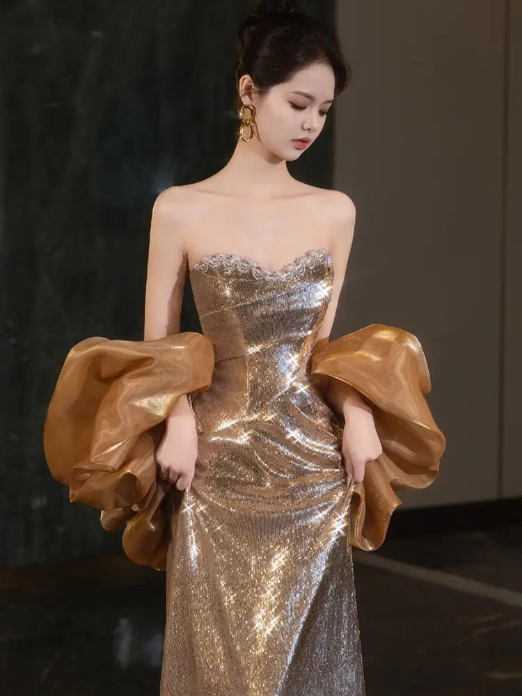 A gold sequin evening gown featuring a strapless design with shimmering sequins and dramatic voluminous satin puff sleeves.
