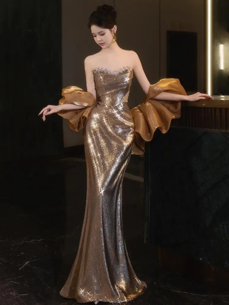 A shimmering gold sequined mermaid evening gown featuring dramatic voluminous satin puff sleeves.