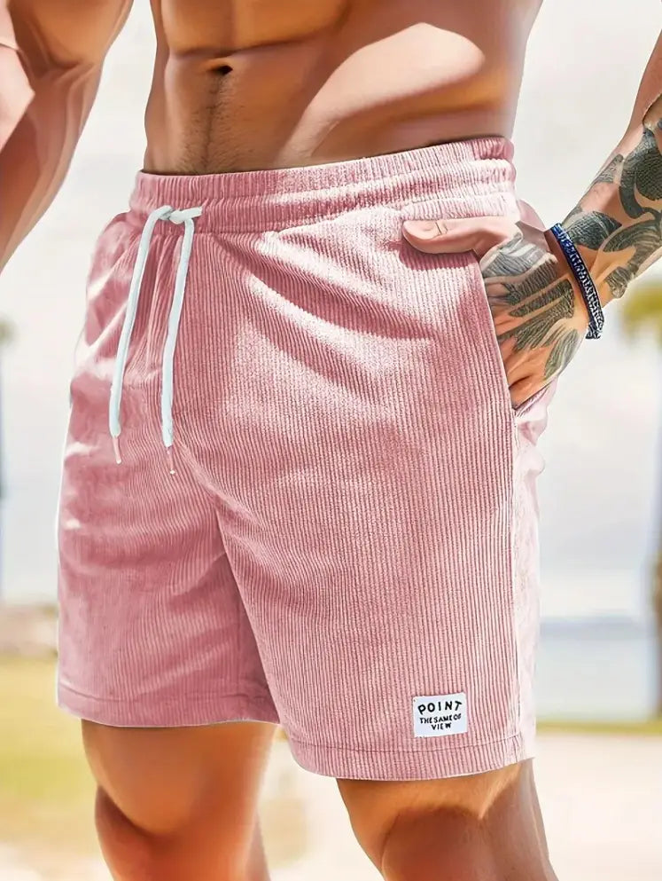 Shorts en velours côtelé rose à cordon de serrage pour hommes, avec des cordons de serrage blancs et une petite étiquette de marque « point » sur la partie inférieure droite de la jambe, conçus comme des pantalons de sport.