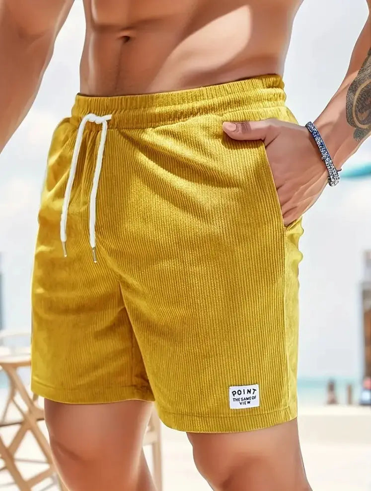 Shorts en velours côtelé jaune à cordon de serrage pour hommes, avec des cordons de serrage blancs et une petite étiquette blanche sur la partie inférieure droite de la jambe, conçus pour un usage sportif.