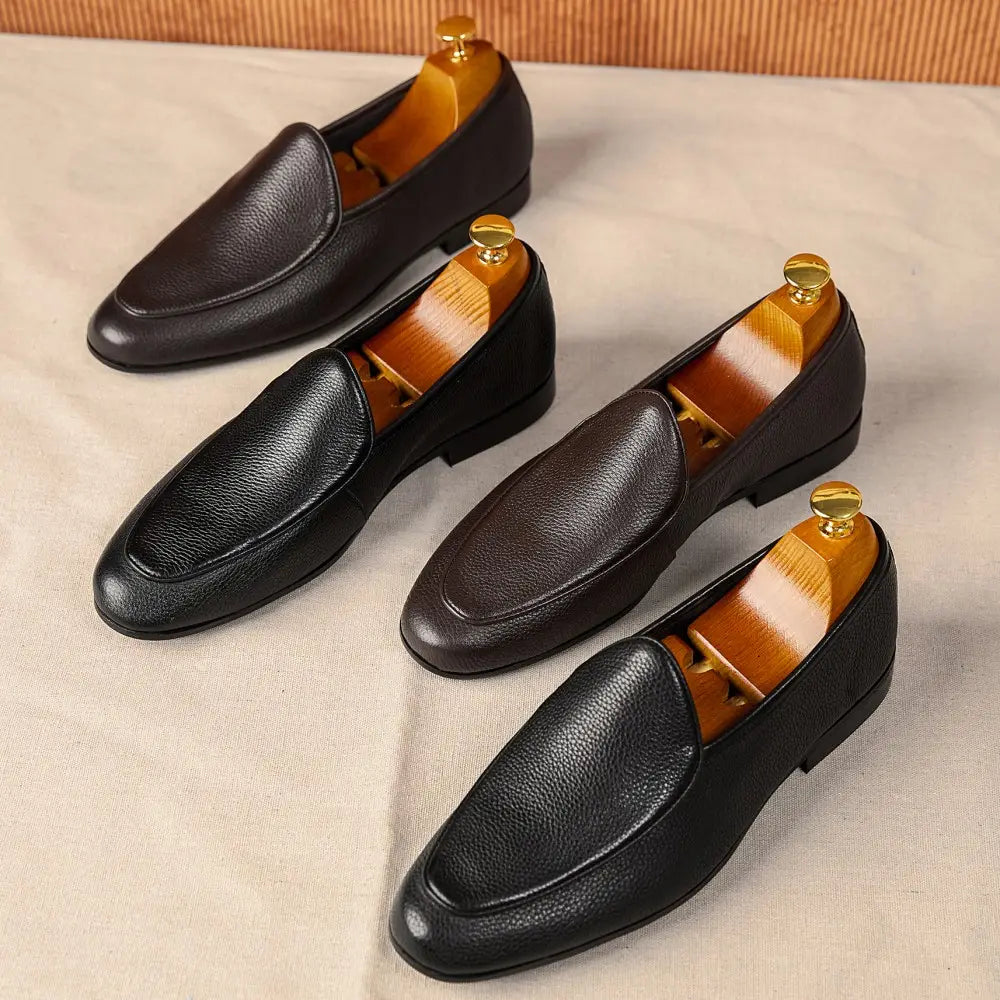 Black leather pointed toe loafers with textured cowhide and pebbled finish featuring gold-toned wooden shoe trees inside.
