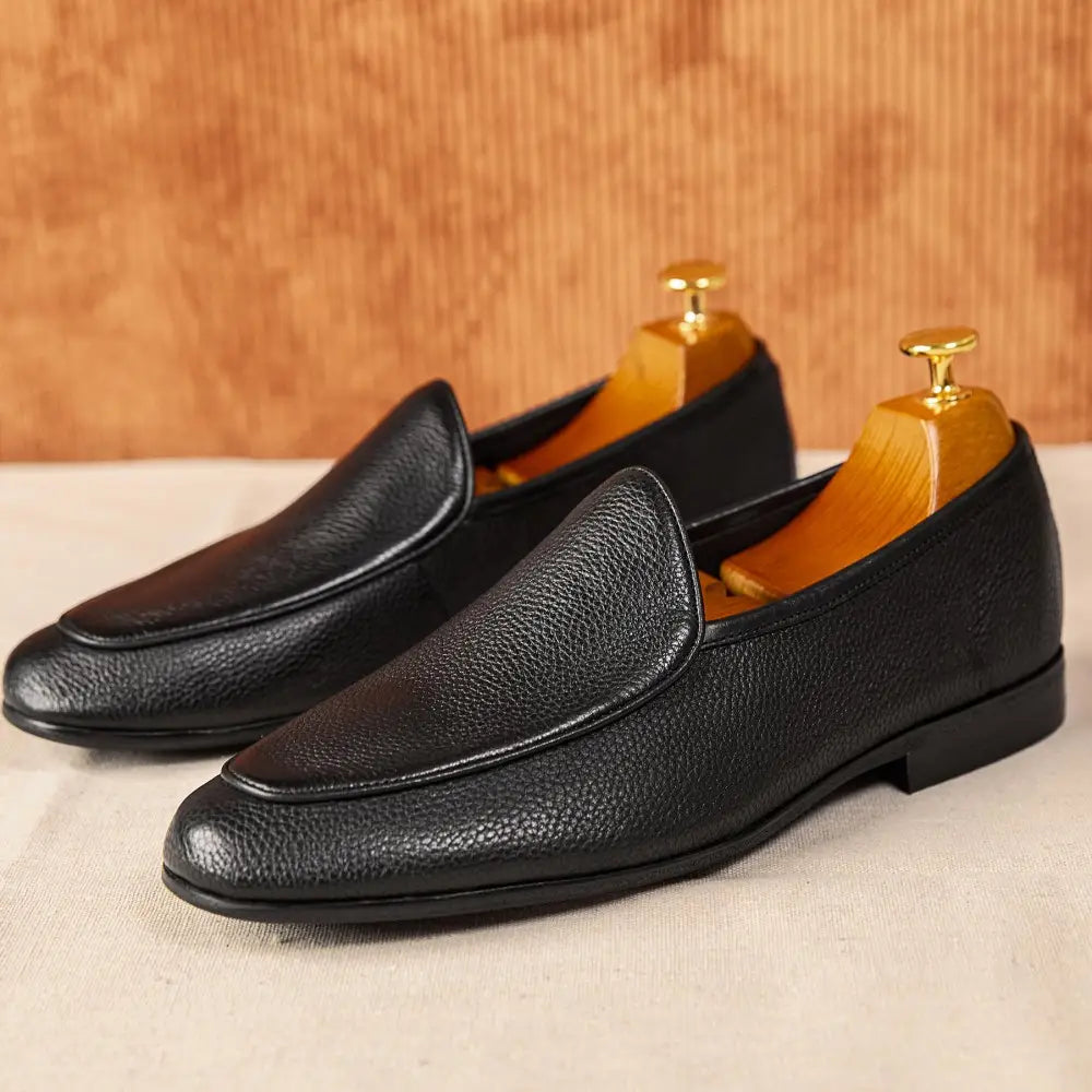 Black leather loafers with pebbled cowhide texture and classic pointed toe slip-on design.