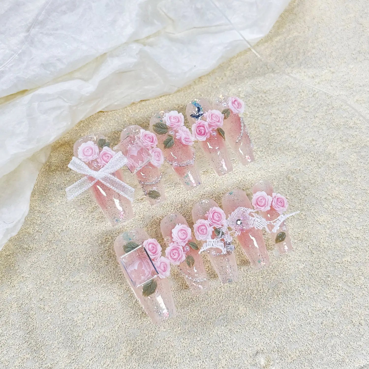 Handmade pink floral acrylic almond press on nails featuring delicate rose embellishments and glittery accents.