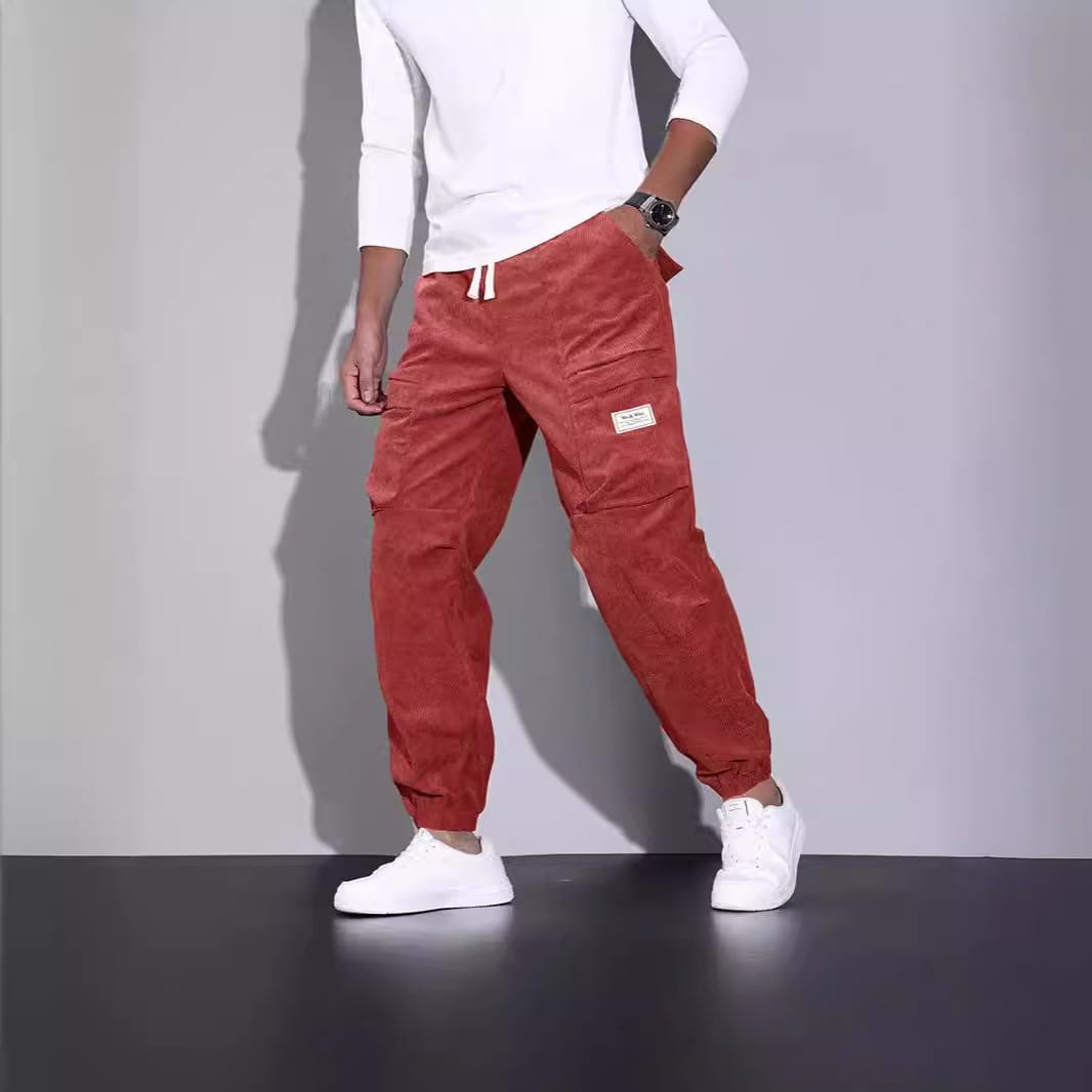 Men corduroy cargo pants in crimson with a drawstring waist, multiple pockets, and a small rectangular brand patch on the thigh for casual loose fit.