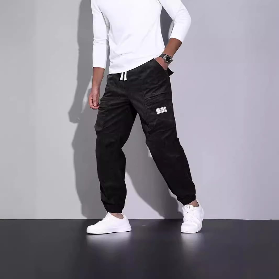 Men corduroy cargo pants in black with white drawstrings and a small rectangular patch on the thigh designed for loose casual wear.