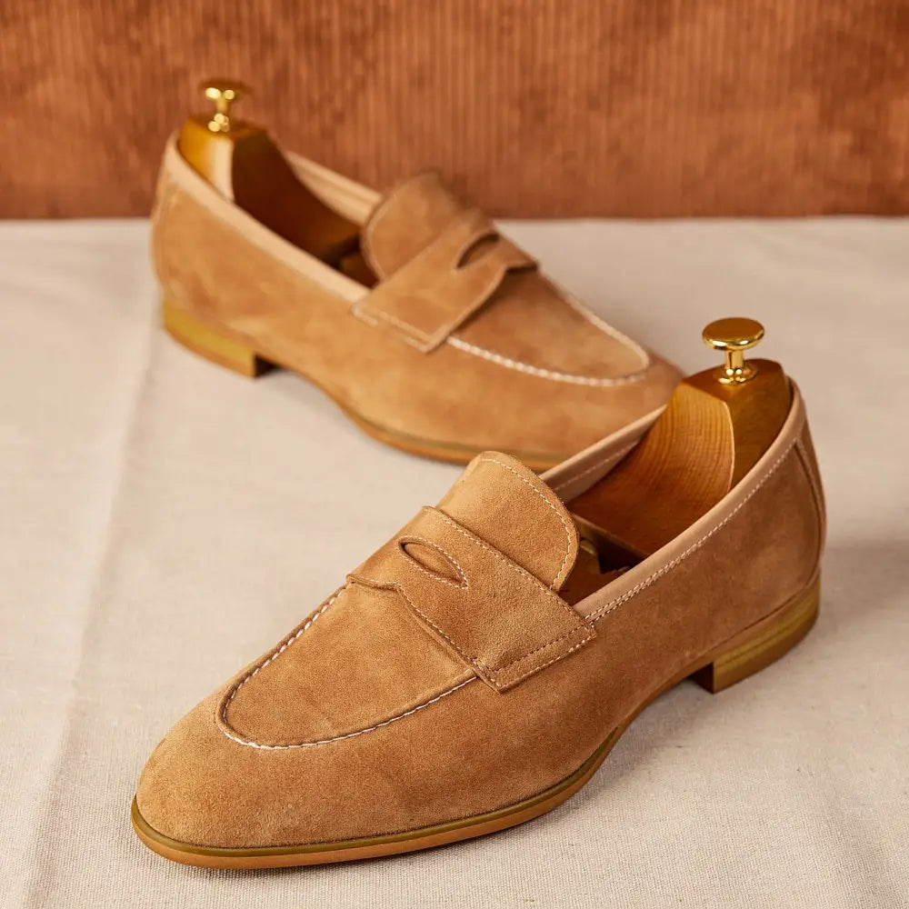 Chaussures de type loafers en suède couleur camel au design classique de penny loafer avec surpiqûres contrastantes blanches et des semelles en cuir brun clair.