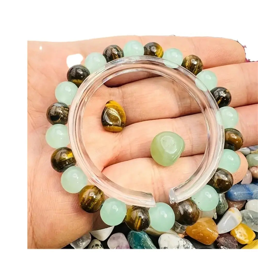 A hand holds a natural tiger eye and green aventurine beaded bracelet featuring alternating round translucent light green jade and golden-brown tiger eye stones.