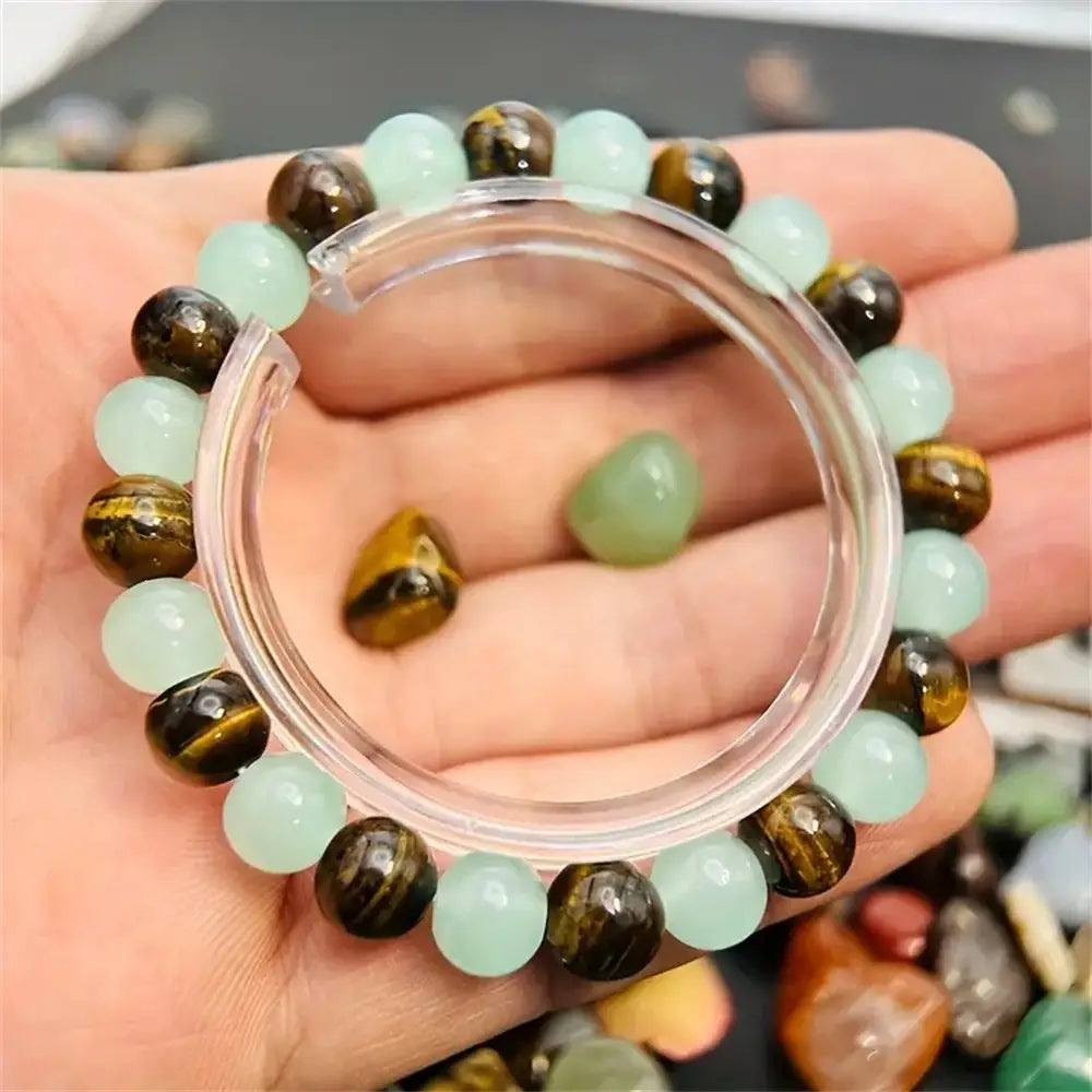 A hand holds a natural tiger eye and green aventurine beaded bracelet featuring alternating round translucent light green jade beads and polished tiger eye stones with golden brown stripes.