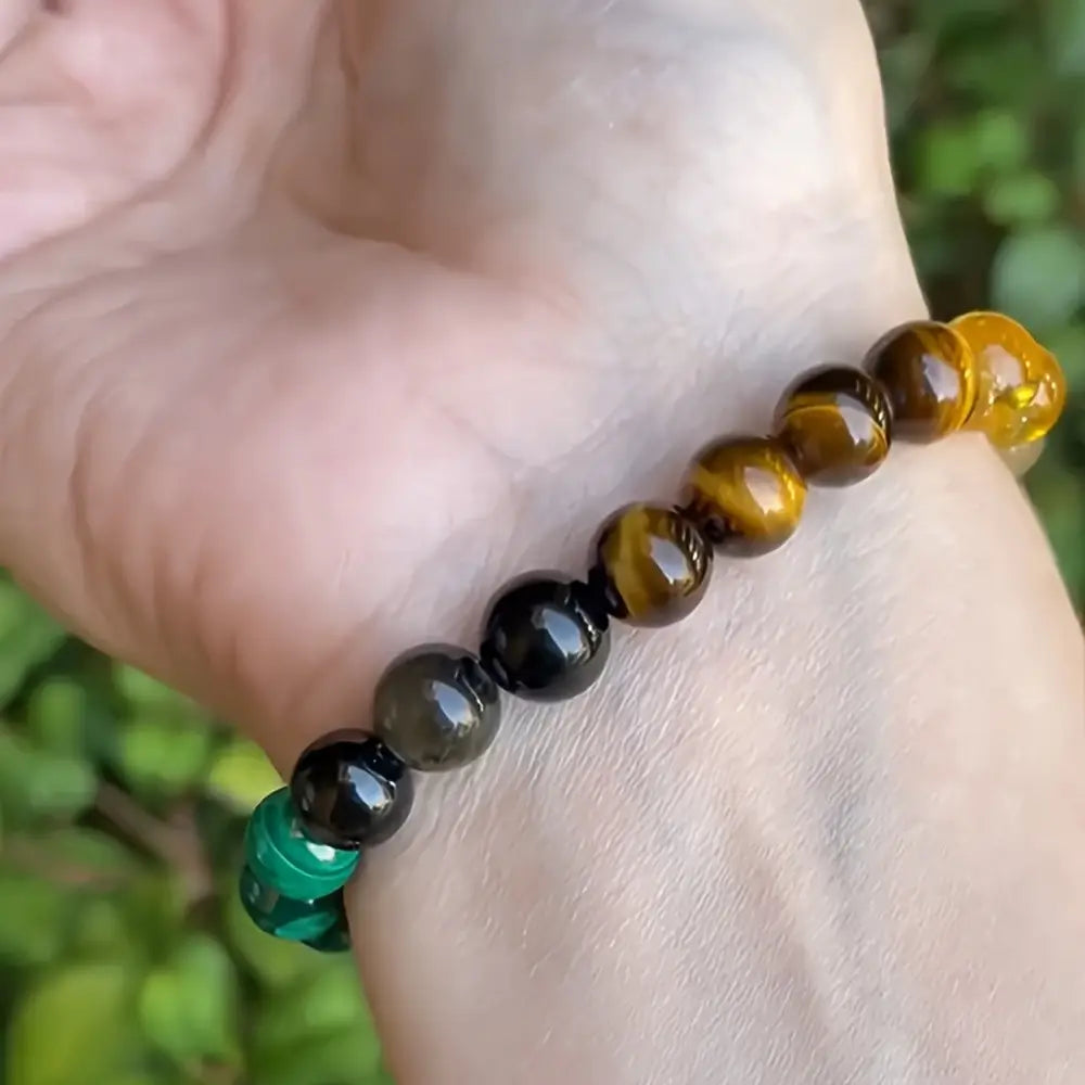 Natural multi-gemstone beaded bracelet featuring polished spherical beads in alternating bands of golden tiger eye, deep black obsidian, and vibrant green malachite with healing crystals.