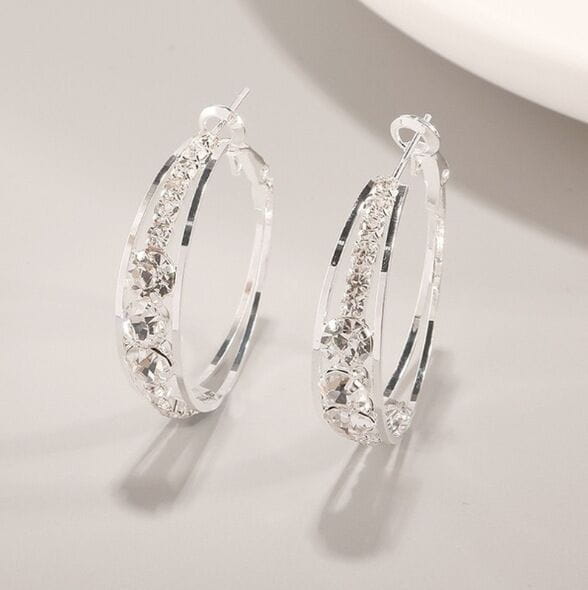 Boucles d’oreilles créoles géométriques en argent serties de cristal pour femmes, ornées de cristaux transparents étincelants le long des bords incurvés.