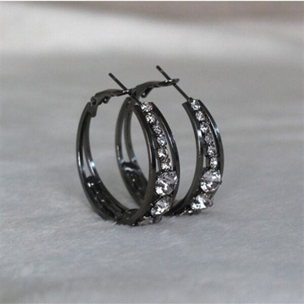 Boucles d’oreilles créoles noires pour femmes, ornées de rhinestones transparents étincelants le long de la courbe dans un design géométrique à base d’incrustation de cristal.