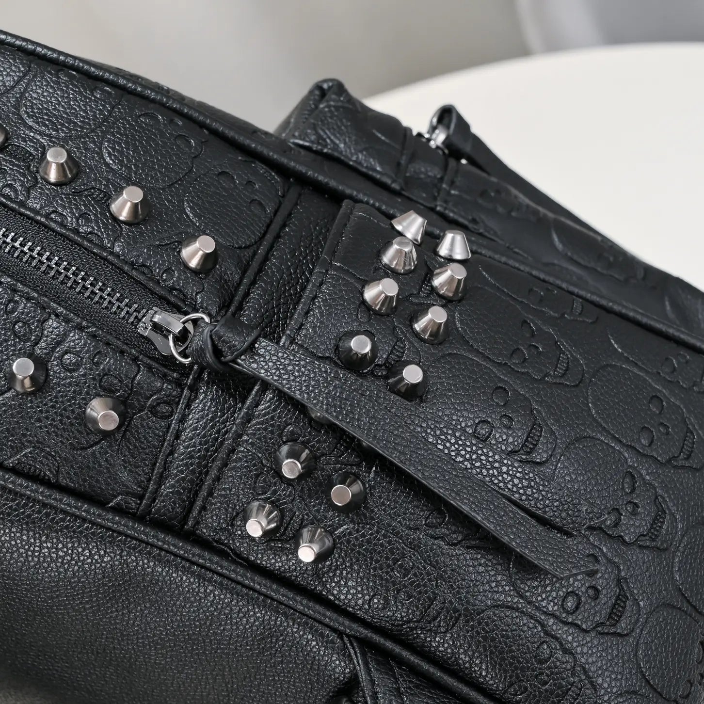 Black studded skull leather commute backpack featuring a black leather crossbody bag with an embossed skull pattern and silver toned studs.