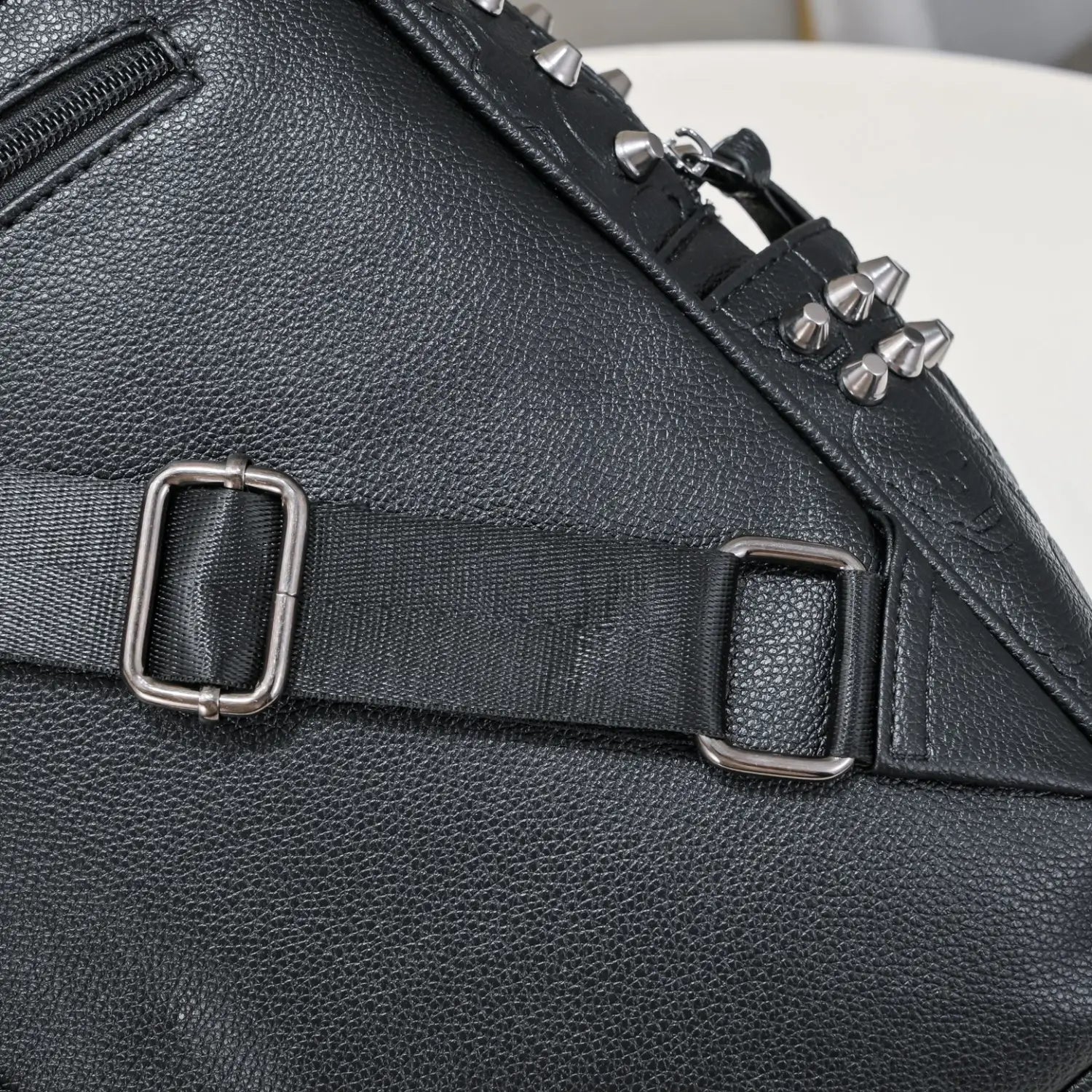 Black studded skull leather commute backpack in black textured leather with silver toned metal studs and adjustable strap buckle shown from the back side.