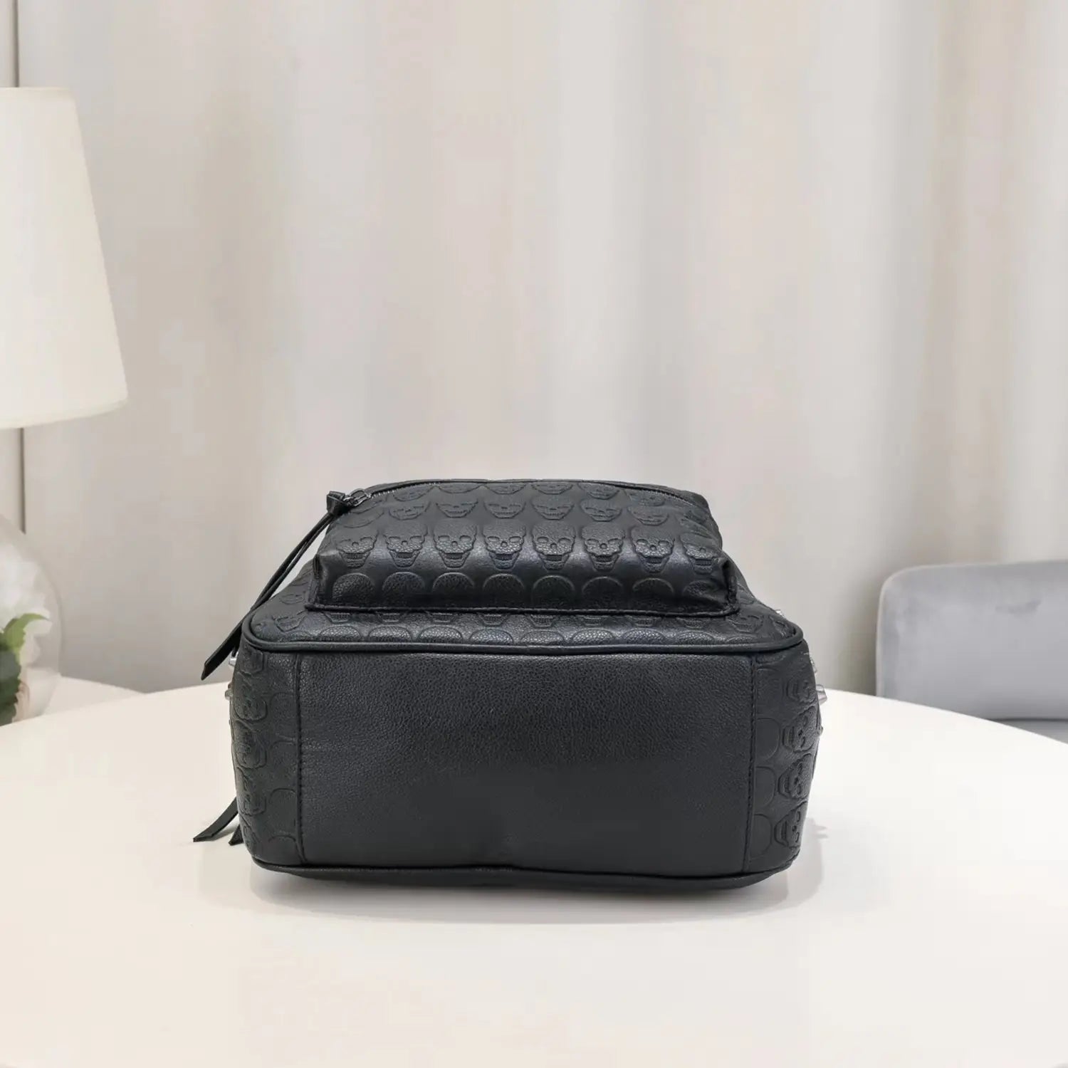 Black leather commute backpack featuring embossed skull pattern and studded details across its surface.