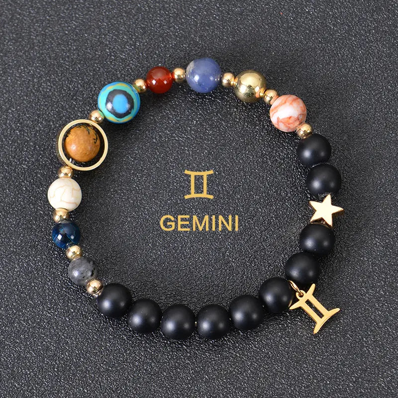 A gemini-themed celestial zodiac planet matte stone beaded bracelet featuring black matte beads, colorful turquoise and red gemstones, gold-toned metal accents with a star charm and the gemini zodiac symbol.