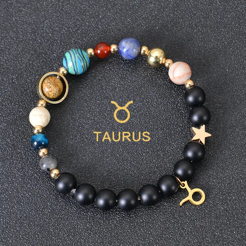 A Taurus-themed celestial zodiac planet matte stone beaded bracelet featuring black matte beads, colorful blue, red, and pink gemstone-like spheres, and gold-toned metallic accents including a star charm and zodiac symbol.