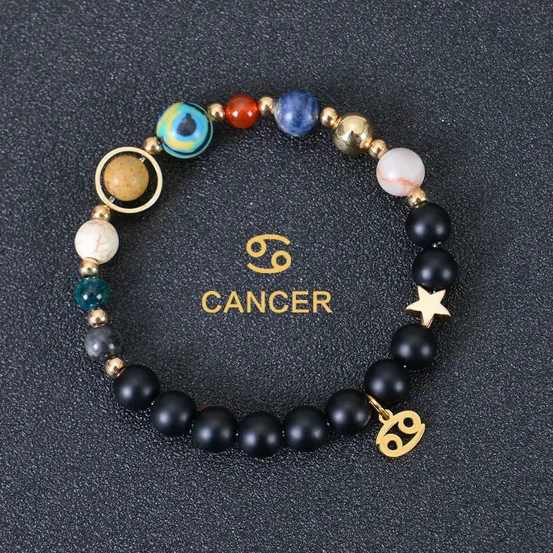 Celestial zodiac planet matte stone beaded bracelet featuring black matte stones colorful gemstones with a blue and green eye-like bead gold-toned metal accents a star charm and a cancer symbol pendant.