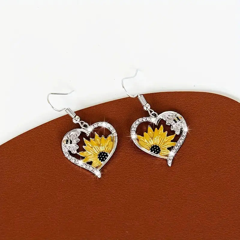 Silberne herzförmige Ohrringe mit einem leuchtend gelben Sonnenblumenmotiv mit schwarzem Zentrum, funkelnden Strasssteinen und zarten Blattdetails im Design der Bienen- und Sonnenblumen-Herz-Strassstein-Silberohrringe.