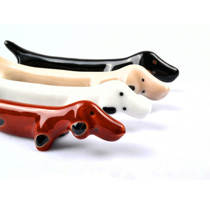 Set aus vier glänzenden Keramik-Stäbchenhaltern in Dackelform, als Wursthund-Deko gestaltet, in Rot, Weiß, Beige und Schwarz.
