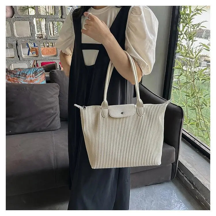 Cream-colored pleated shoulder tote bag made of canvas with minimalist design and silver-toned metal hardware.