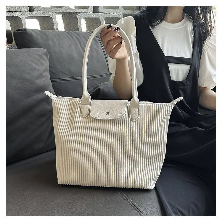 Cream-colored ribbed leather minimalist tote bag with matching handles and a flap closure suitable for shoulder carry.