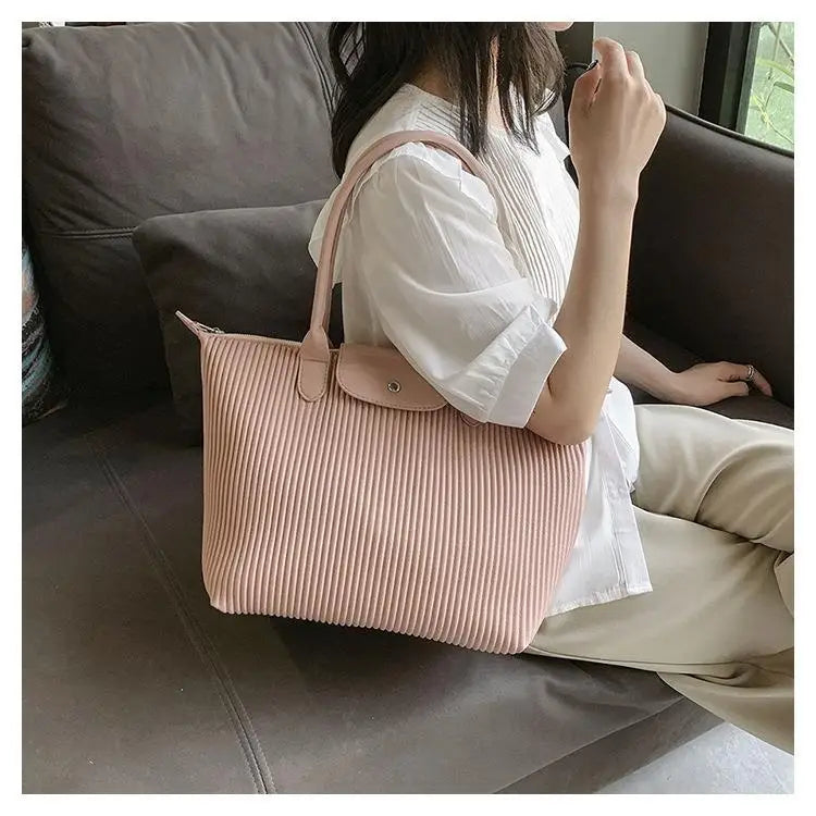 A soft pink pleated shoulder bag made of minimalist pu leather with a matching top handle and small flap closure.