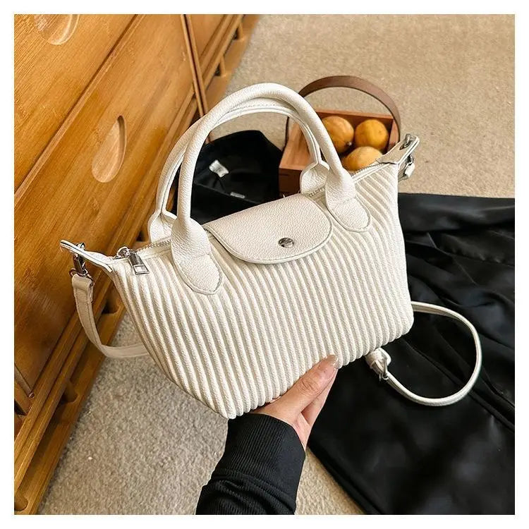 A cream-colored pleated shoulder bag made of ribbed pu leather with a flap closure and silver hardware.