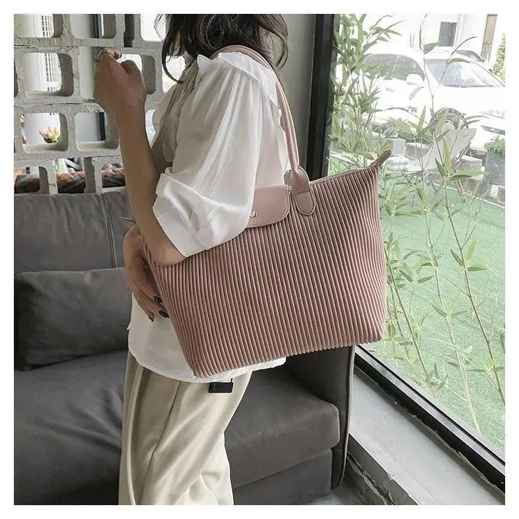 A soft pink pleated shoulder tote bag made of corduroy with matching pu leather handles and a front flap closure.