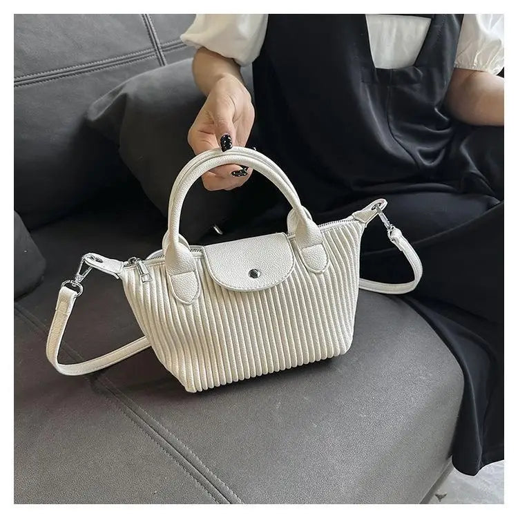 White ribbed leather pleated shoulder bag with top handle and adjustable strap in minimalist pu leather tote design.