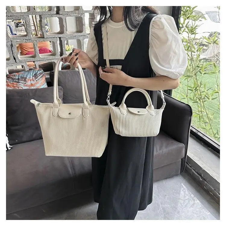 Cream-colored ribbed pu leather tote bag with a classic fold-over flap and top handles designed as a minimalist pleated shoulder bag.