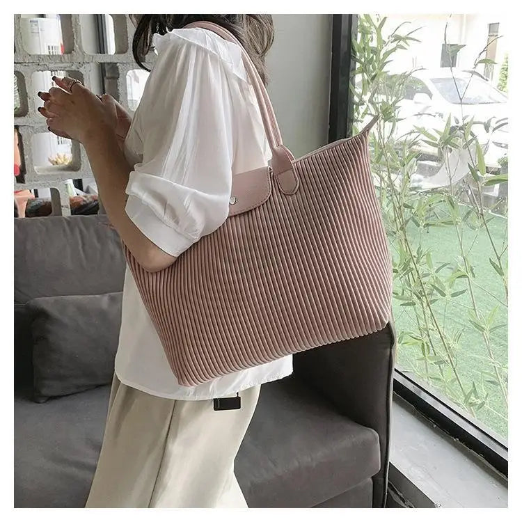 A soft pink pleated shoulder tote bag made of corduroy with a matching leather handle and flap closure.