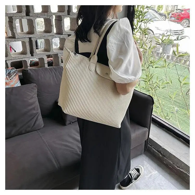 Beige pleated tote bag made of minimalist pu leather featuring black straps and a matching leather flap closure.
