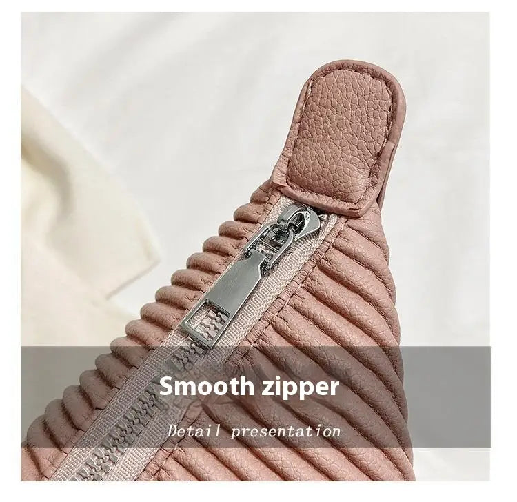 A pink quilted leather zipper pull with a silver toned metal slider on a pleated shoulder bag minimalist pu leather tote.