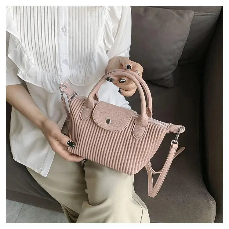 A soft pink pleated shoulder bag made of ribbed pu leather with a top handle and detachable strap suitable as a minimalist tote.