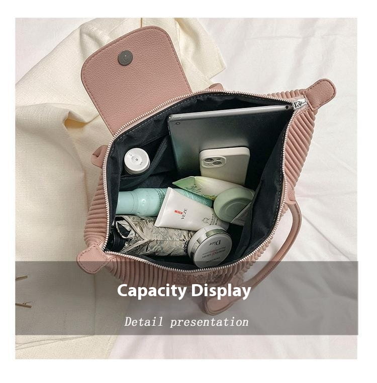 A soft pink pleated shoulder bag minimalist pu leather tote with ribbed texture and matching flap and zipper, filled with toiletries and tech accessories.