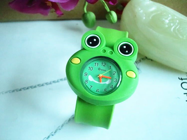 Montre-bracelet en silicone à l’effigie d’un animal en 3D, style dessin animé, pour enfants, avec un bracelet en silicone souple vert en forme de grenouille et un cadran rond avec des aiguilles orange.
